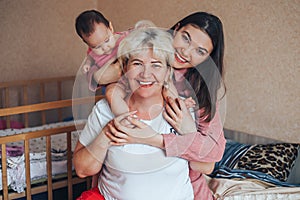 Little cute girl, her attractive young mother and charming grandmother are spending time together at home