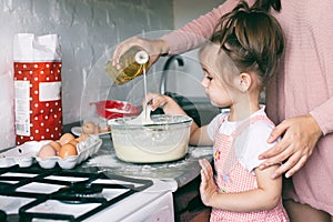 A little cute girl and her mother preparing the dough in the kitchen at home