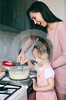 A little cute girl and her mother preparing the dough in the kitchen at home