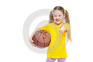 Little cute girl holding a basketball in her hand and showing a like gesture. Isolated on white background.