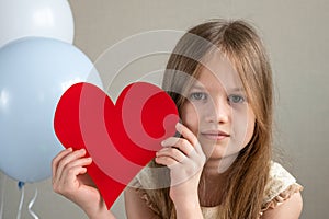 Little cute girl holding big red heart near air balloons. Valentines Day, love, mothers fathers Day, romantic concept