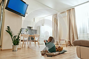 A little cute girl holding a gamepad playing videogames on a TV while sitting on a floor cross-legged