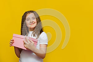 Little cute girl holding gift box on Yellow background