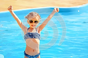 Little cute girl holding hands up near a swimming pool