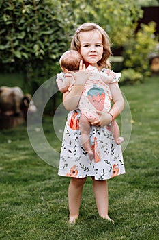Little cute girl is holding a newborn sister in her arms and spending happy time with her outdoors