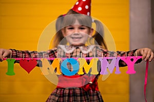 Little cute girl holds a garland with text `I love mommy` of colorful paper alphabet