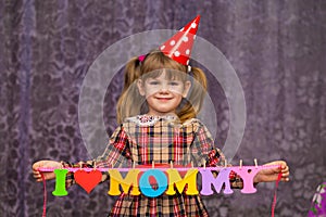 Little cute girl holds a garland with text `I love mommy` of colorful paper alphabet