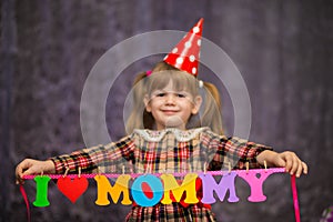 Little cute girl holds a garland with text `I love mommy` of colorful paper alphabet