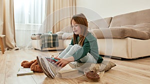 A little cute girl hutting a gamepad on her feet smiling sitting on a floor of a big guestroom