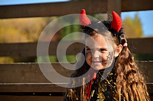 little cute girl in the image devil on Halloween. red horns on the head with black grimm for halloween zombie