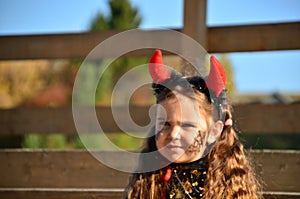 little cute girl in the image devil on Halloween. red horns on the head with black grimm for halloween zombie