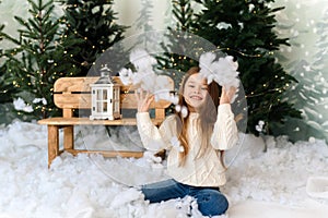 A little cute girl in the interior of the Christmas studio throws artificial snow and rejoices at Christmas eve.