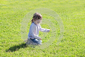 Little cute girl in jeans sitting on grass