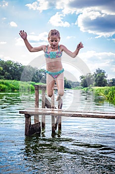 Little cute girl jumping off the dock into a beautiful river at