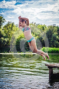 Little cute girl jumping off the dock into a beautiful river at