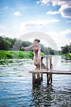 Little cute girl jumping off the dock into a beautiful river at sunset