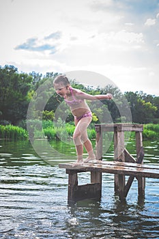 Little cute girl jumping off the dock into a beautiful river at sunset