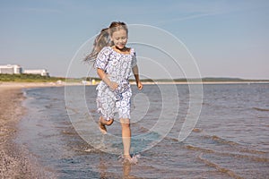 Little cute girl with lond hair in beautiful dress running on sea beach during summer holiday.Child playing on ocean beach. Sea