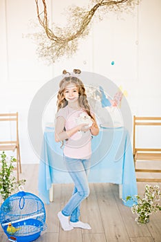Little cute girl with long curly hair with little bunnies and Easter decor at home at the  table.