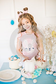 Little cute girl with long curly hair with little bunnies and Easter decor at home at the  table.