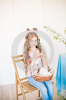 Little cute girl with long curly hair with little bunnies and Easter decor at home at the  table.