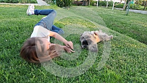 little cute girl lying on green grass, lawn. sunset. summer. a happy child plays with his little dog. friendship between child and