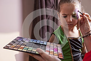 Little cute girl making facepaint before halloween party