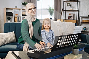 Little cute girl with music muslim teacher having lesson at piano at school of music.