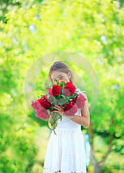 Little cute girl with peony flowers. Child wearing white dress playing in a summer garden. Kids gardening. Children play outdoors