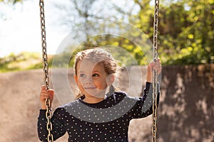 Little cute girl with pigtails smiling rides on a swing in polka dot clothes in the park against the background of foliage