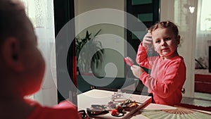 Little cute girl in pink dress combs her hair with comb