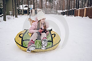 Little cute girl in pink warm outwear having fun rides inflatable snow tube in snowy white cold winter outdoors. Family sport