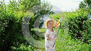 A little cute girl playing with a colorful pinwheel in the garden on a warm day.