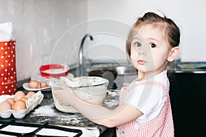 A little cute girl preparing the dough in the kitchen at home