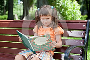Little cute girl preschooler with book on bench