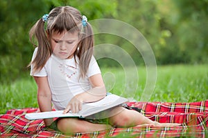 Little cute girl preschooler with book in park