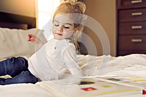 Little cute girl reading book on bed