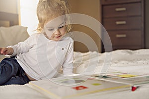 Little cute girl reading book on bed