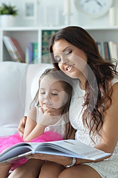 Little cute girl reading book with mother while sitting on safe