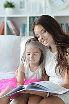 Little cute girl reading book with mother while sitting on safe