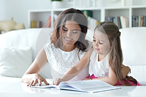 Little cute girl reading book with mother at the table