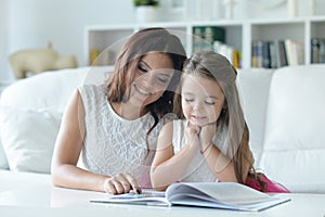 Little cute girl reading book with mother at the table