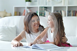 Little cute girl reading book with mother at the table