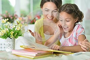 Little cute girl reading book with mother at the table at home