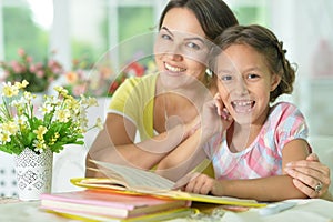Little cute girl reading book with mother at the table at home
