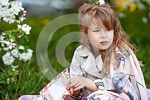 Little cute girl  reading a book  in the park. Child outdoors in blossoming spring garden