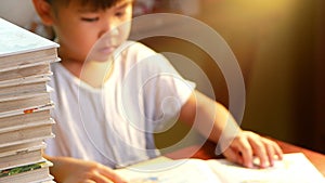 A little cute girl reading a book sits on table at home. Stay at home to quarantine from coronavirus pandemic. Homeschool concept.