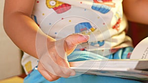 A little cute girl reading a book sits on table at home. Stay at home to quarantine from coronavirus pandemic. Homeschool concept.