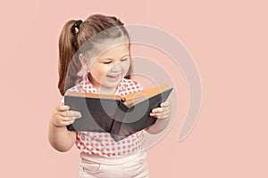 Little Cute Girl Reading Book And Smiling on Pink Background