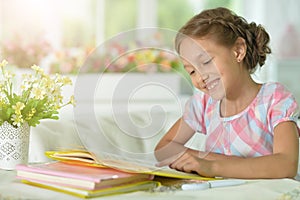 Little cute girl reading book at the table at home